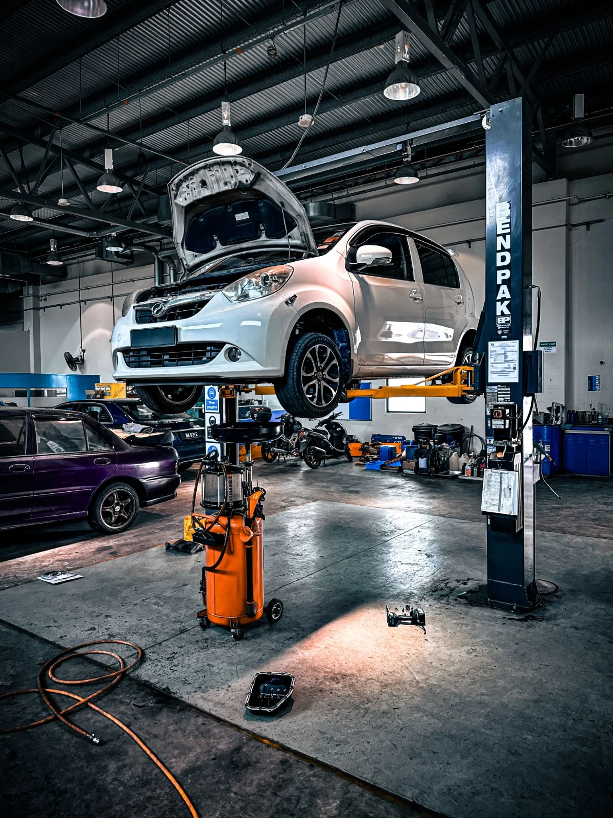 A white vehicle raised on a workshop lift with its bonnet open